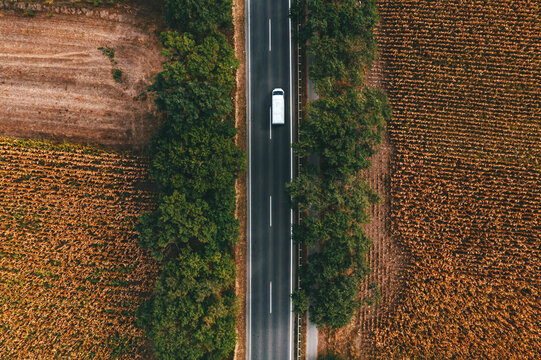 White commercial van vehicle driving along the highway road through countryside landscape, aerial shot from drone pov