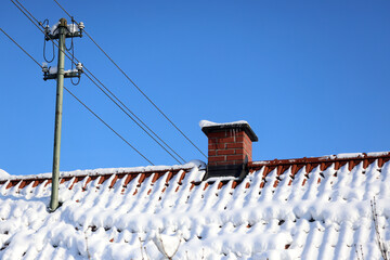 Urban air pollution, Smoke coming out of a brick chimney on a tiled roof with snow on in winter, bright sunshine, blue sky, 