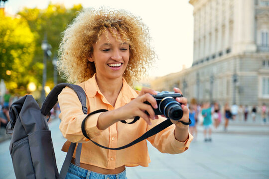Brazilian female tourist smiling and taking photos with a camera while sightseeing in Madrid, Spain.