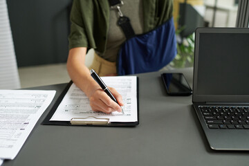 Close-up of young woman with injury filing documents while sitting in bureaucratic office