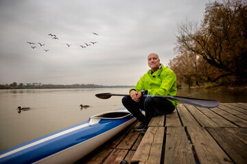 A middle-aged man sitting on the jetty and ready to go kayaking