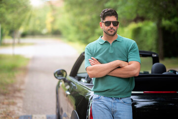 A caucasian man standing next to his convertible car on the street