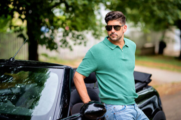 A caucasian man standing next to his convertible car on the street - 687890563