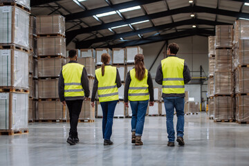 Rear view of warehouse workers walking in warehouse. Team of warehouse workers preparing products for shipment.