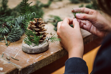 Kind, Kinderhände basteln Weihnachtsgeschenk aus Naturmaterialien, Tannenzweig, Holzscheibe und...