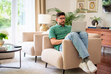 Confident mid aged man sitting in an armchair at home and using laptop for work