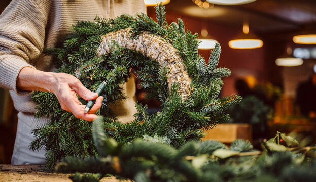 H&auml;nde halten Draht und Adventskranz. Mensch bastelt einen weihnachtlichen Adventskranz.