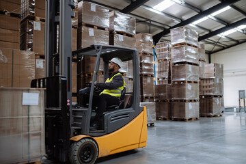 Multiracial warehouse worker driving forklift. Warehouse worker preparing products for shipmennt, delivery, checking stock in warehouse. - obrazy, fototapety, plakaty