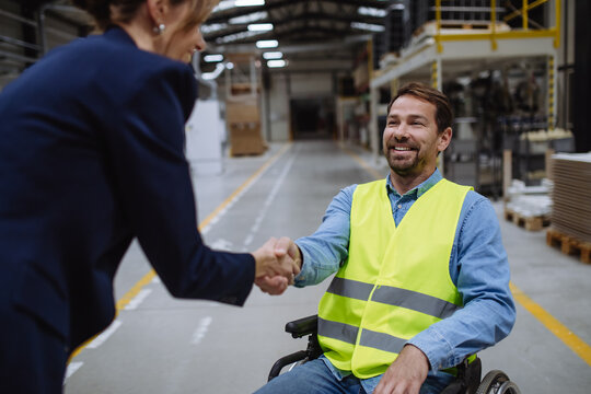Portrait of man in wheelchair working in warehouse, shaking hand with HR manager, director. Concept of workers with disabilities, accessible workplace for employees with mobility impairment.