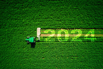 2024 Happy New Year concept and agricultural tractor mowing green field aerial view