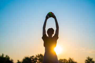 silhouette of a young woman doing yoga with a ball against the backdrop of the rising sun early in...
