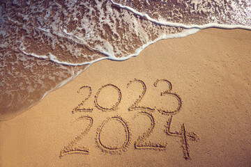 Starting new year 2024 ending 2023 text on the beach sand and splashing sea wave seasonal background