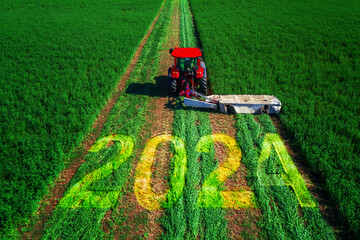 2024 Happy New Year concept and agricultural tractor mowing green field aerial view.
