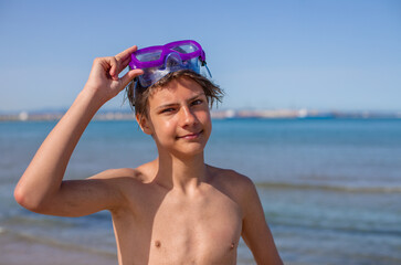 A smiling young teenager with a diving mask reflects the pure joy of summer by the ocean.