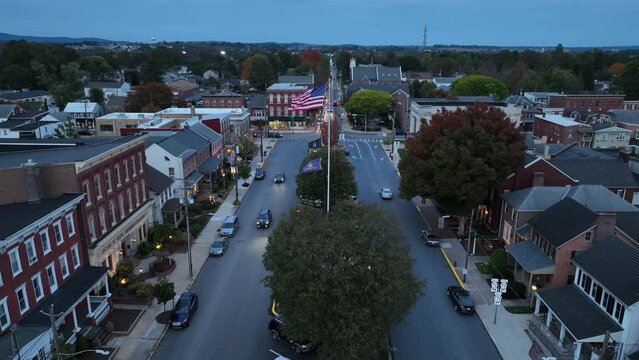American flag waving in town square during dusk. Fast aerial descending shot.