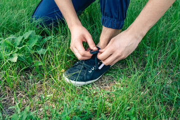 A young man sits on the fresh, green grass, tying the laces of his sneaker