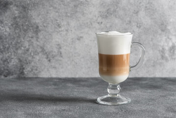 Latte coffee layered with milk foam in a glass on a gray concrete background. Side view. Copy space