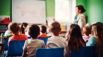 Back view of group of kids children at desks, paying close attention to teacher in school classroom