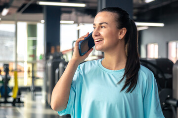 Happy young woman athlete talk on a phone at gym, copy space.