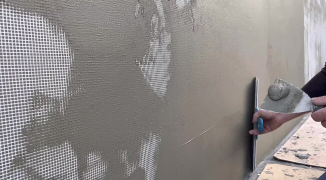 Close-up of a wall being puttied by hand with a putty knife. The facade reinforcing mesh is puttied before finishing the wall. Repair of apartments, residential premises. Repair the walls.