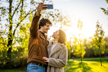Portrait of happy loving couple in park in sunset. They are taking selfie.