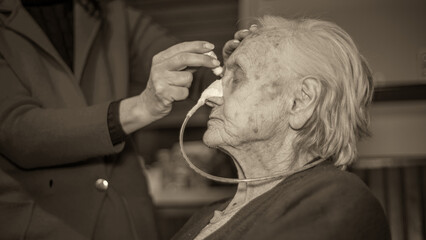 An elderly woman with a food cannula in her nose gets medication at home