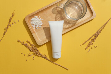 Wooden tray featured a handful of white rice, glass of water and a cosmetic tube. Few wheat ears displayed. Natural beauty blank label for branding mock-up concept