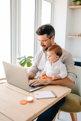 Father working with his baby boy in home office with laptop. Work from home concept	