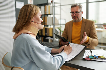 Young woman with injury of neck filing insurance documents during her meeting with manager in office