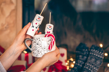Festive Christmas cup of hot drink with marshmallow snowmen in female hands.