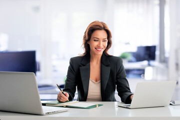 Brunette haired mid aged businesswoman sitting at the office desk and working on laptop