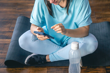 A woman sits on a mat and uses a smartphone, online workout concept.
