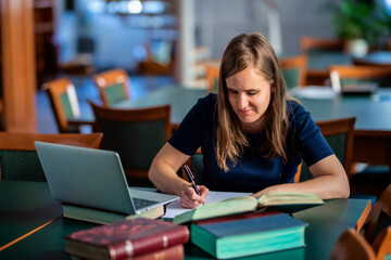 A visually impaired woman sitting and studying in the university library - obrazy, fototapety, plakaty