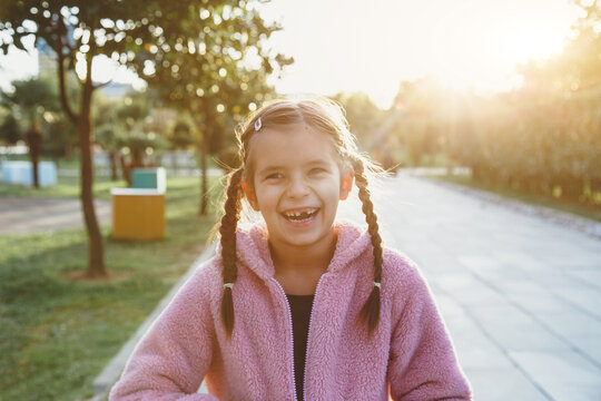 portrait of a laughing funny cheerful girl 6 years old in the park at sunset, missing front tooth.