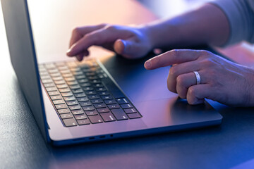 A man uses a laptop at night, close-up of his hands.