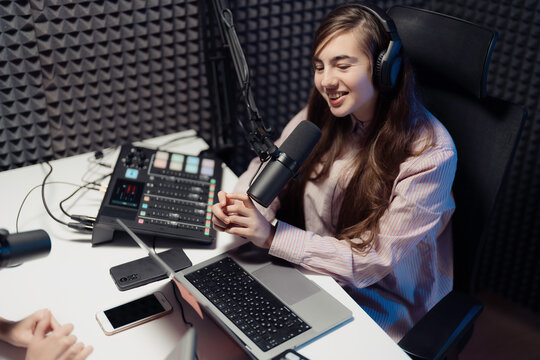 Smiling female podcaster in a striped shirt speaking into a microphone, fully equipped with podcasting gear studio