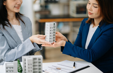 Real estate broker agent presenting and consult to customer to decision making sign insurance form agreement, home model, concerning mortgage loan offer.