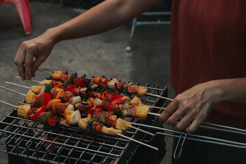 Naklejka premium People are cooking seafood and vegetable skewers on a charcoal grill. with a plate of shrimp placed next to it A warm family holiday celebration. BBQ party