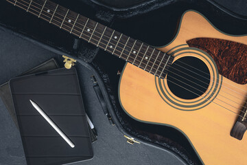 Acoustic guitar in a protective case and a digital tablet, top view.