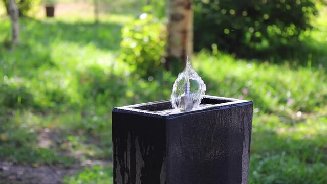 Close-up of a cool water fountain (pulpulak) against a backdrop of lush green trees and grass.