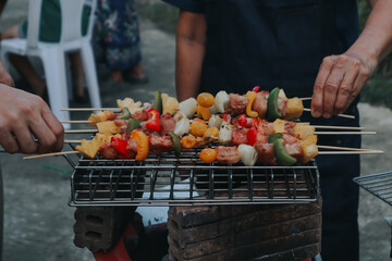 People are cooking seafood and vegetable skewers on a charcoal grill. with a plate of shrimp placed next to it A warm family holiday celebration. BBQ party