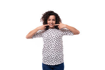 young stylish woman with curly hair dressed in a blouse with polka dots smiles and feels happy