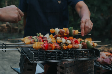 People are cooking seafood and vegetable skewers on a charcoal grill. with a plate of shrimp placed next to it A warm family holiday celebration. BBQ party