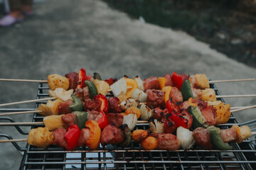 People are cooking seafood and vegetable skewers on a charcoal grill. with a plate of shrimp placed next to it A warm family holiday celebration. BBQ party