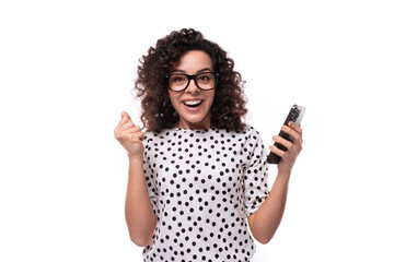 young caucasian businesswoman with curly hair dressed in a blouse with polka dots holds a smartphone