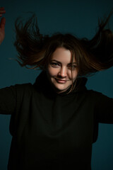 Classic dark studio portrait of a young brown-haired woman in black clothes sitting on a chair.