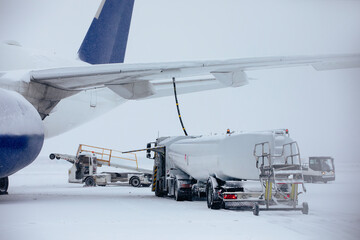 Refueling of airplane from fuel tanker truck at airport during snowfall. Ground service before flight on frosty winter day..