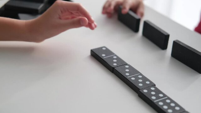 Children play dominoes. Board games for preschoolers. Close-up of children's hands playing dominoes on a white table.