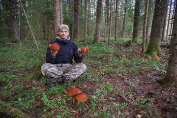 A European man, age 45, sits in a louse on the ground and holds edible mushrooms in his hands....