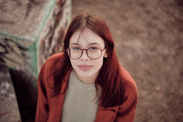 Teenage girl with glasses and red coat looking at camera. High angle view.